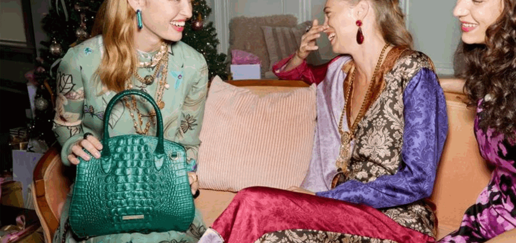 Woman holding a mystic green croc embossed leather satchel with structured shape and top handles