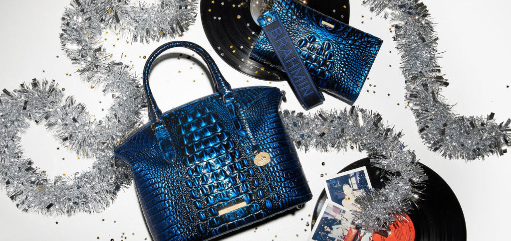 Brahmin sapphire blue croc-embossed satchel paired with a matching blue wristlet, styled on a festive white background with vinyl records, silver tinsel, and scattered gold star confetti.