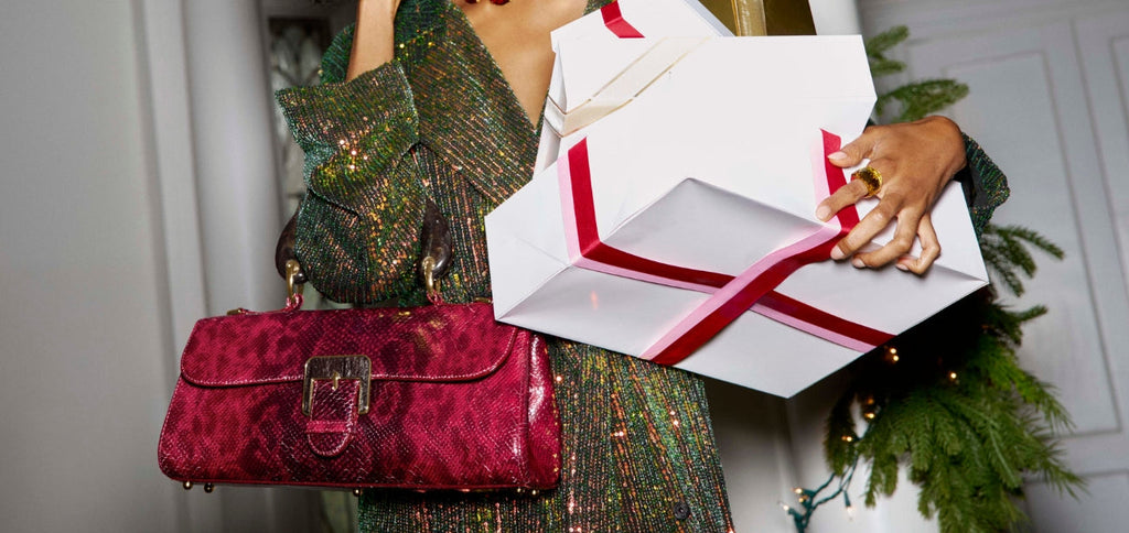 Woman holding holiday gifts while wearing a Brahmin red textured leather shoulder bag with gold hardware.