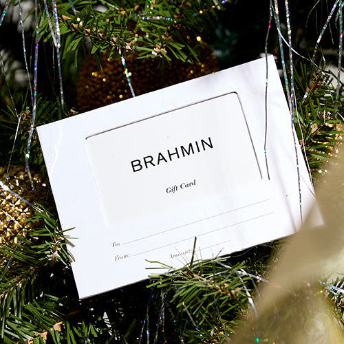 Brahmin gift card inside a white envelope with the Brahmin logo, nestled among evergreen branches of a decorated holiday tree.