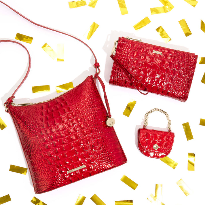 Brahmin red handbag accessories featuring a shoulder bag, wristlet and mini bag with glossy embossed texture and gold tone hardware surrounded by gold confetti.
