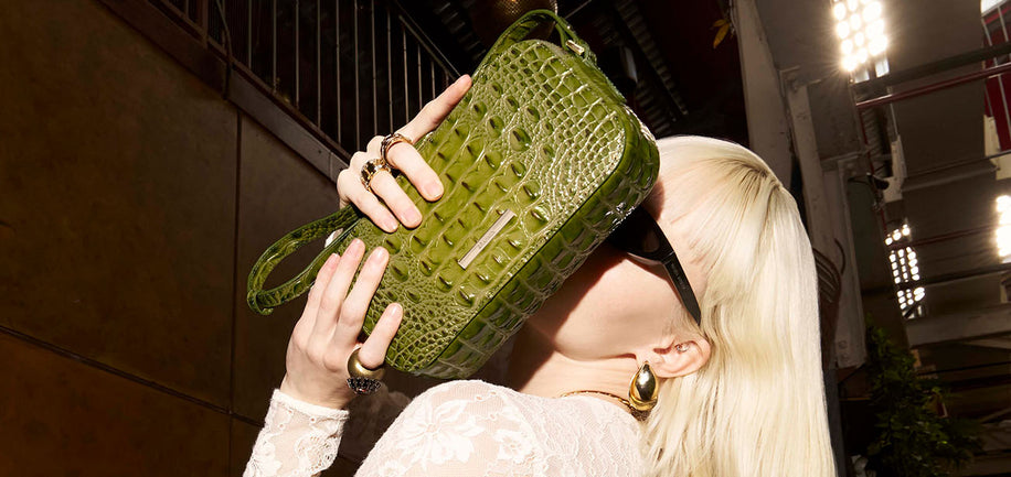 Woman holding a green crocodile-patterned handbag in an indoor setting