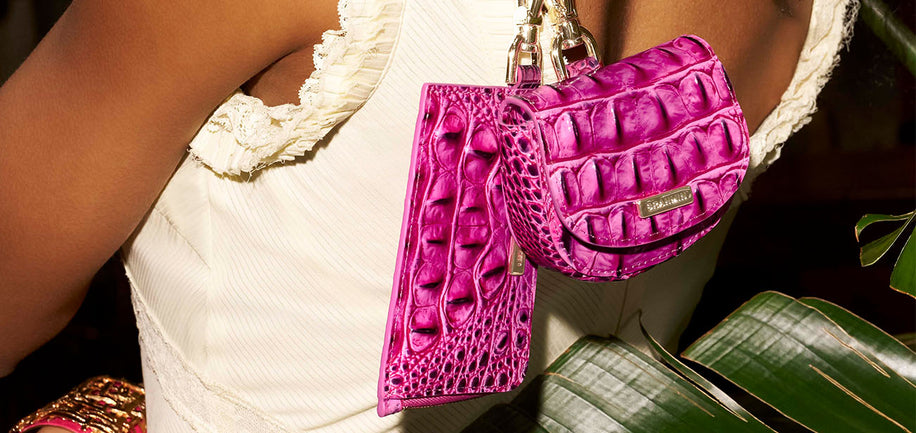 Pink textured handbag accessories held by a person with a white top, green leaves in the background