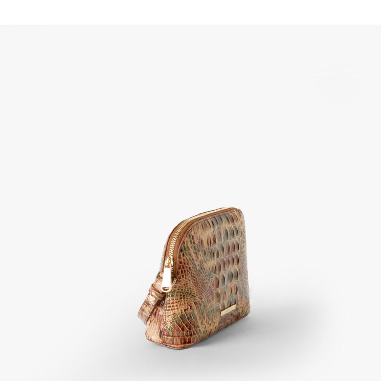 A small dome-shaped crossbody bag with a textured crocodile skin pattern in shades of brown, beige, and muted green, featuring a gold Brahmin plaque on the front. Amal Side View.
