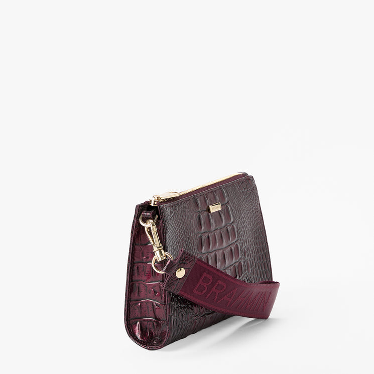 A dark burgundy crocodile-embossed leather clutch bag with a matching leather strap featuring the brand name 'BRAHMIN' in gold-tone lettering, shown on a clean white background.