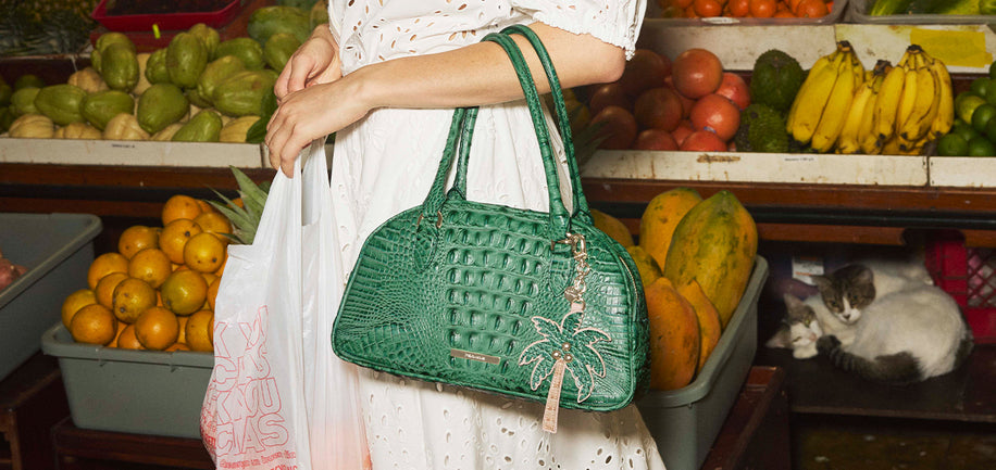 Person holding Angie Palm Alden Road Handbag and palm charm in a market setting.