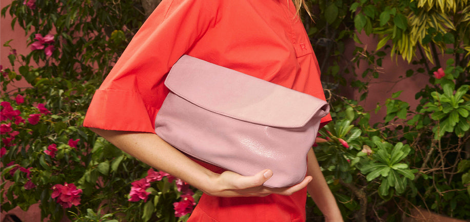 Person holding a pink clutch against a garden background