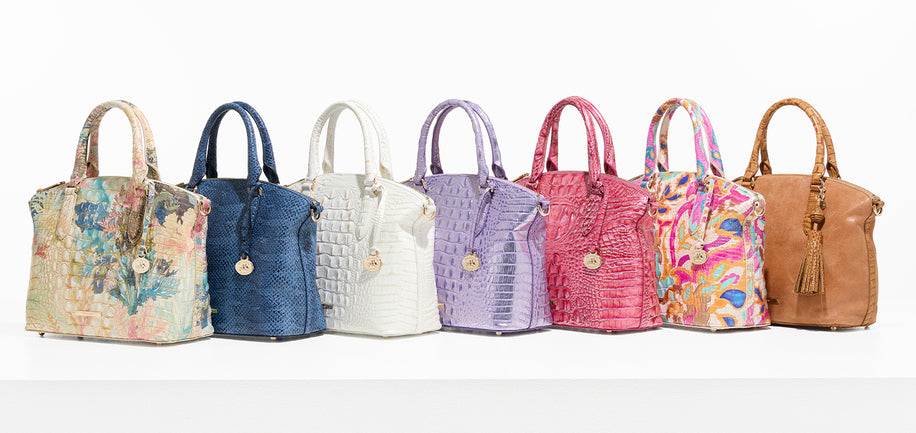 Seven Brahmin satchel handbags displayed side by side in assorted colors and textures including floral print, blue, white, lavender, pink, multicolor, and tan category banner