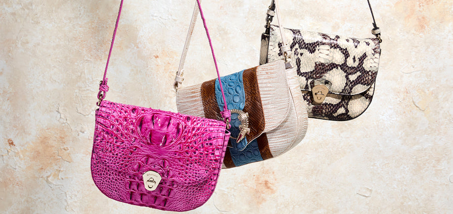 Three Brahmin Portia handbags of different designs and colors hanging against a textured beige background.