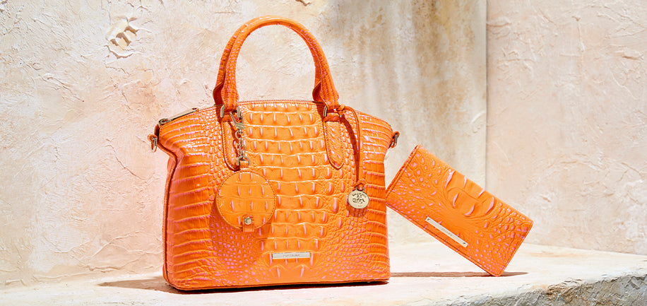 Brahmin bright orange croc embossed leather satchel with matching orange wallet on textured stone background