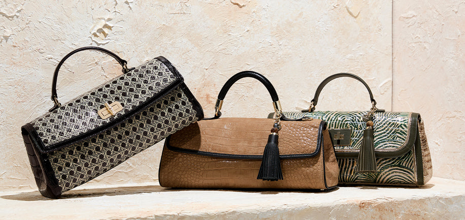 Three handbags of different designs on a stone surface with a textured wall background.