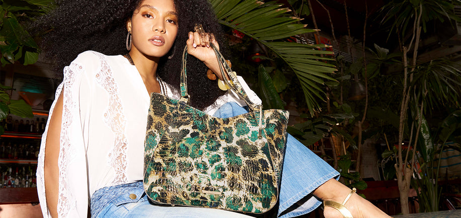 Woman holding a patterned handbag in an outdoor setting with plants.