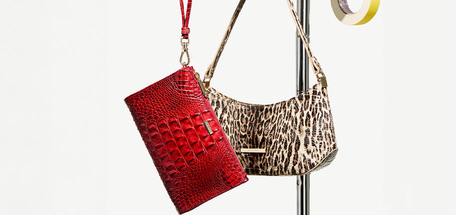 Two handbags hanging from a metal display stand against a plain light background: a bright red crocodile-embossed clutch on the left and a beige-and-black leopard-print shoulder bag on the right.