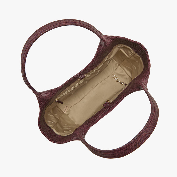 A top-down view of a dark plum purple textured leather handbag, showing its beige interior lining and double shoulder straps on a light gray background.