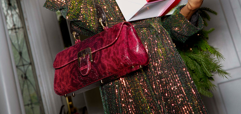Model holding red textured handbag with a sparkling green dress indoors