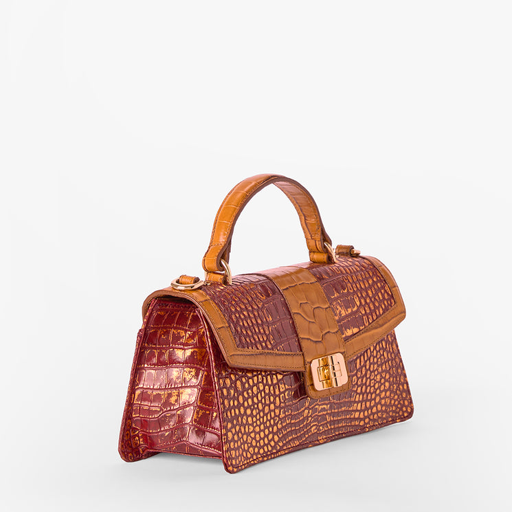 A structured handbag with a glossy reddish-brown crocodile-embossed texture, featuring a top handle, a front flap with a gold-tone turn-lock clasp, and a smooth tan-brown leather trim.