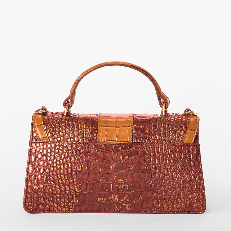 A structured top-handle handbag with a crocodile-embossed texture in a reddish-brown tone, featuring tan leather trim and a central strap detail, set against a plain light gray background.