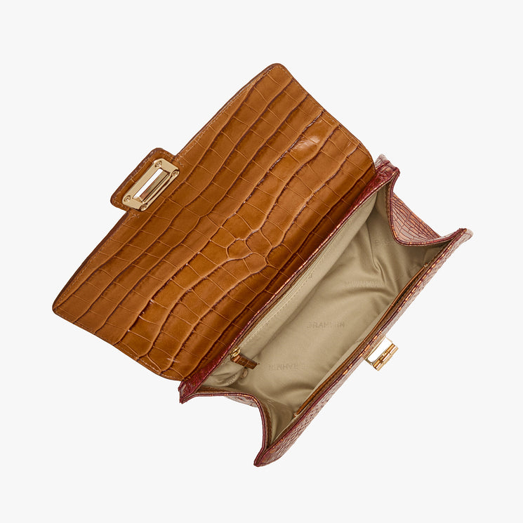 A brown crocodile-embossed leather clutch bag shown open from a top-down view, revealing a beige interior lining and gold-tone hardware, set against a plain white background.