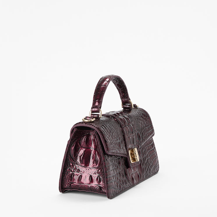 A structured top-handle handbag in glossy embossed crocodile leather, shown on a plain white background. The bag is a deep plum purple with gold-tone hardware.