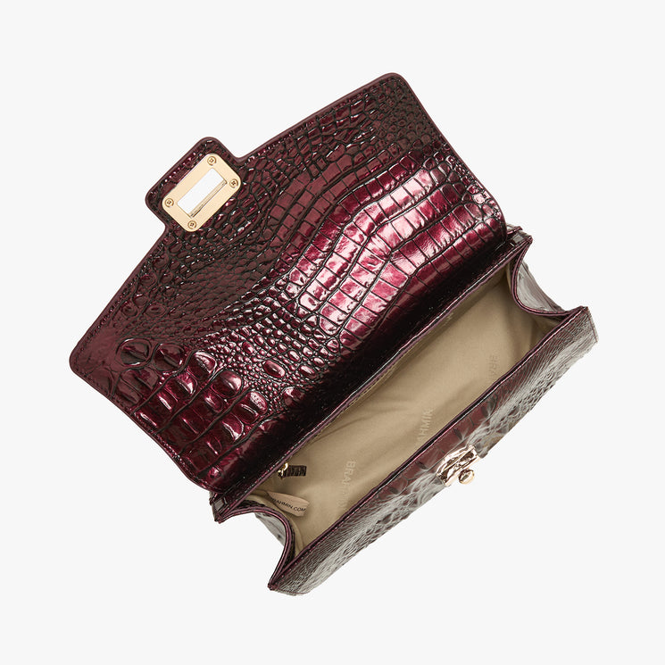 A dark burgundy crocodile-embossed leather clutch bag, shown open to display its interior lining and gold-tone hardware, set against a plain light gray background.