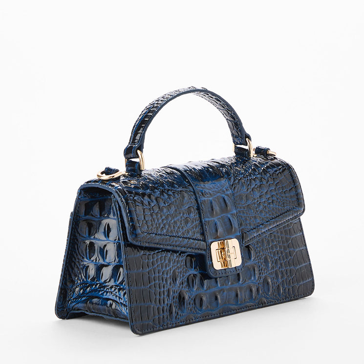 A small structured handbag with a glossy crocodile-embossed texture in deep blue, featuring a top handle, gold-tone hardware, and a front flap closure. Side view.