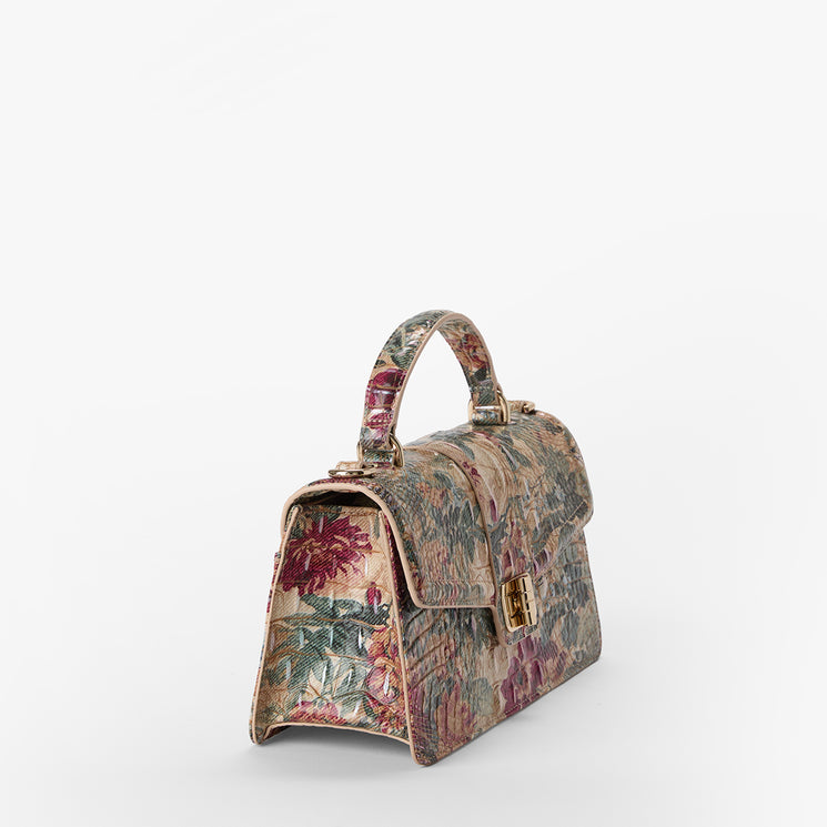 A structured top-handle handbag with a vintage floral tapestry pattern in muted red, green, and beige tones, featuring gold-tone hardware and a flap closure, photographed on a clean white background.