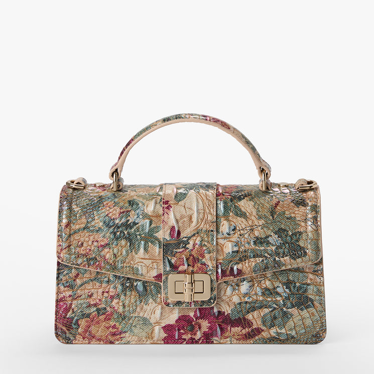 A structured handbag with a top handle, featuring a complex floral and botanical print in muted tones of beige, green, and burgundy, accented by gold-tone hardware.
