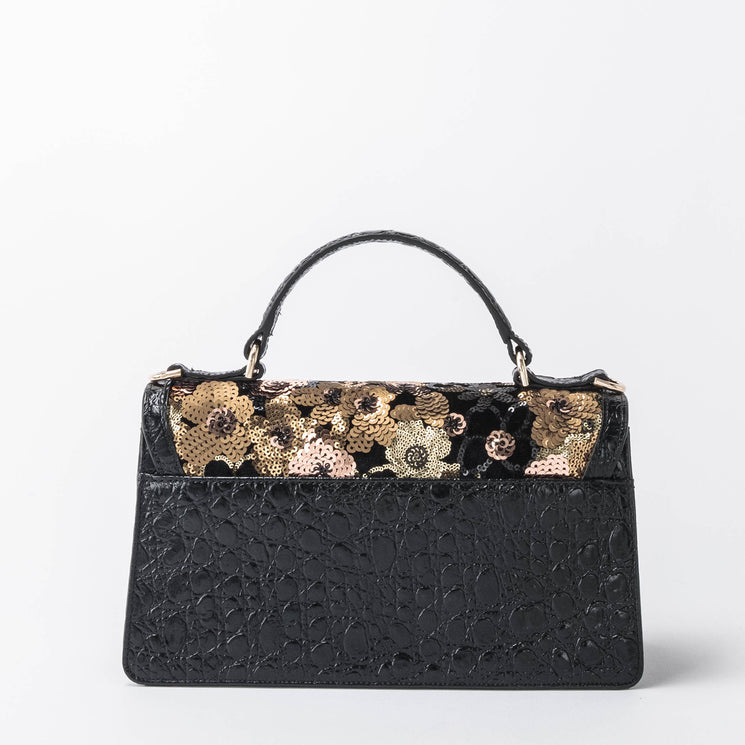 BRAHMIN Genie black vintage-inspired satchel with textured finish, short handle, and gold, black, and silver floral sequins near the top. Bag shown on a plain white background.