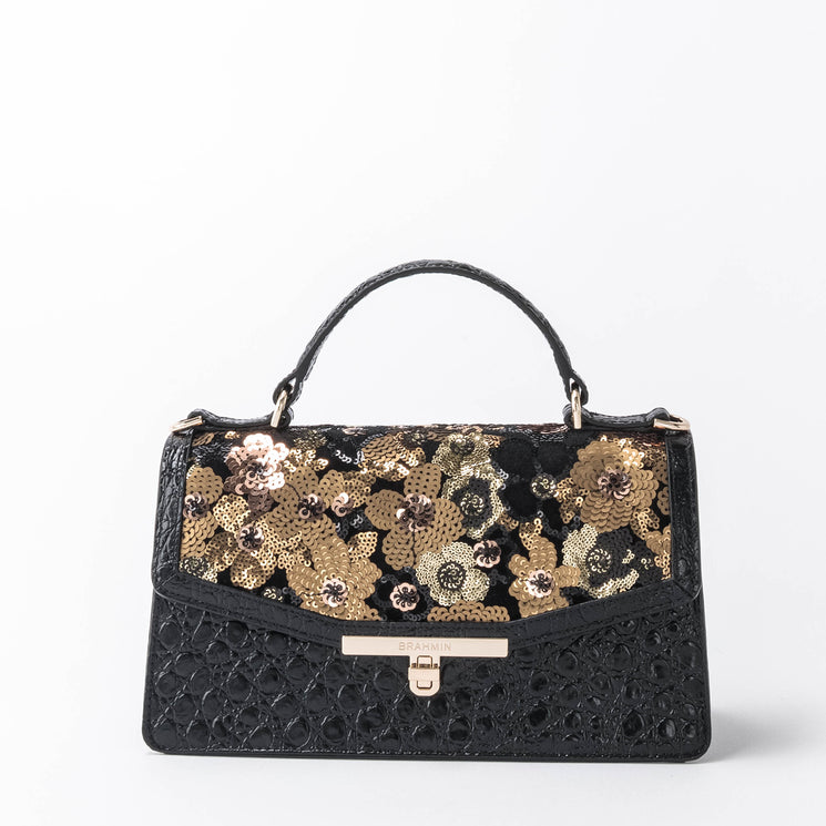 BRAHMIN Genie satchel in black with vintage-inspired shape, gold and bronze sequin floral pattern, single top handle, textured base, metal clasp closure, and signature BRAHMIN logo plate.