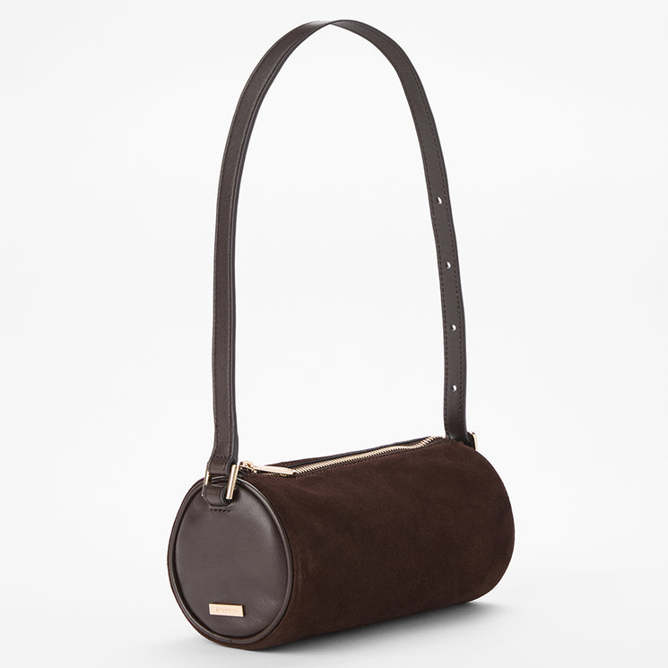 A dark brown cylindrical shoulder bag made of suede and smooth leather, featuring a gold-tone zipper and a small gold brand plaque, set against a plain white background.