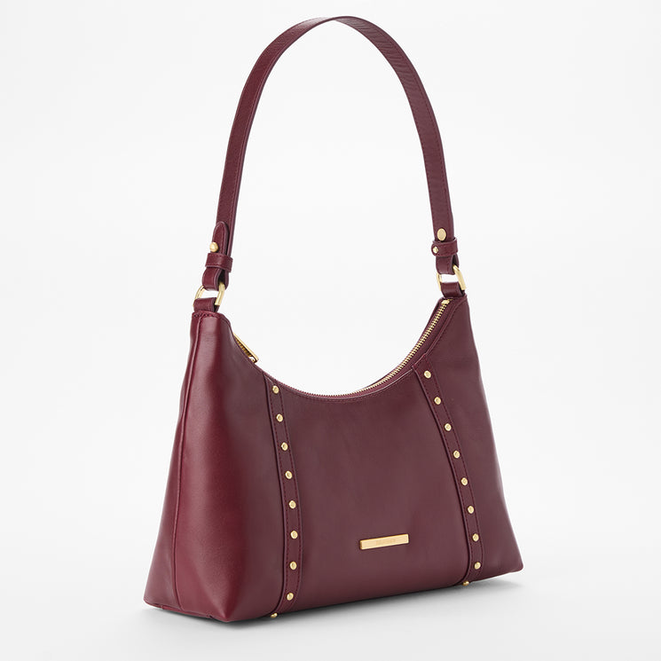 Brahmin maroon leather shoulder bag with gold studs, zipper closure, single shoulder strap, and rectangular gold logo plate on front; shown against a white background, highlighting smooth texture and hardware details.
