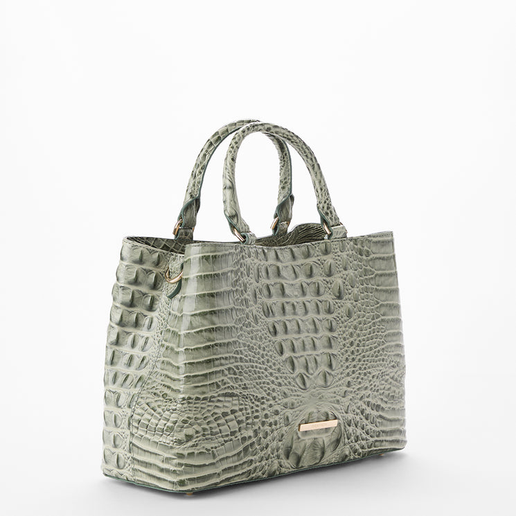 A structured tote handbag with an embossed crocodile skin texture in a muted sage green color, featuring dual top handles and a small gold-tone metal plaque on the front, set against a plain white background.