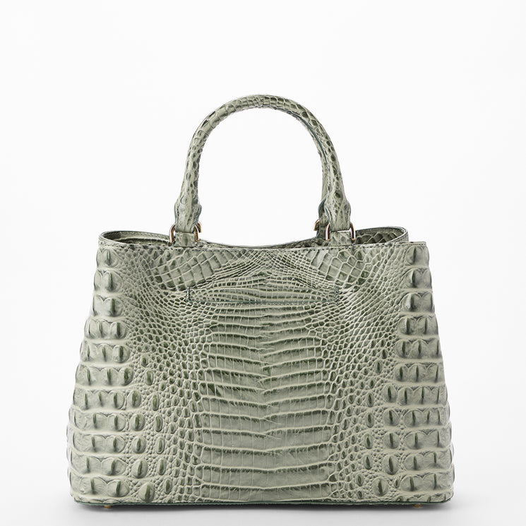 A structured handbag with a crocodile-embossed texture in a muted sage green color, featuring dual top handles and a clean silhouette, set against a plain white background.