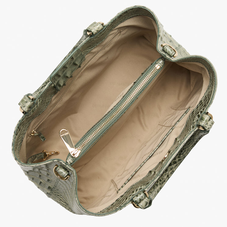An overhead view of a structured handbag made of textured crocodile-embossed leather in a muted sage green, showing the beige interior lining and a central zippered pocket.