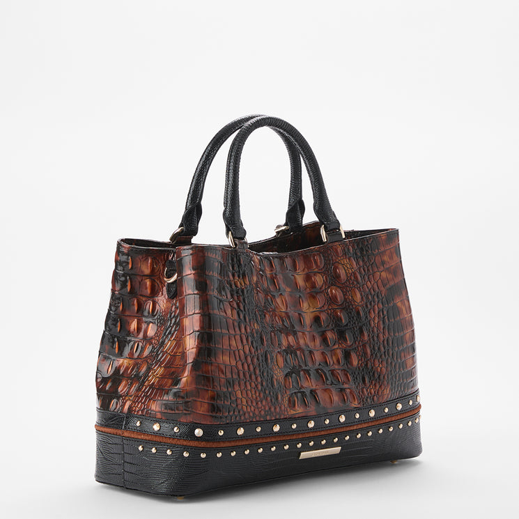 A structured tote handbag with a brown and black crocodile-embossed pattern, featuring black leather handles, a black base with silver studs, and a small gold brand plaque on the front.