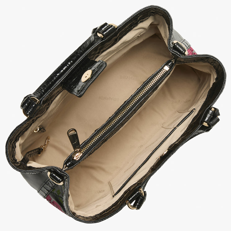 Brahmin structured black handbag with floral textured exterior, gold-tone hardware, top handle, open view showing beige lining, center zip pocket divider, and side compartments. Interior details clearly visible.