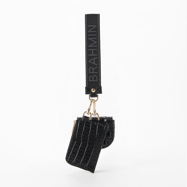A black crocodile-embossed leather key pouch with a matching wrist strap featuring the brand name 'BRAHMIN' in gray lettering, attached with gold-tone hardware, shown against a plain white background. Back view.