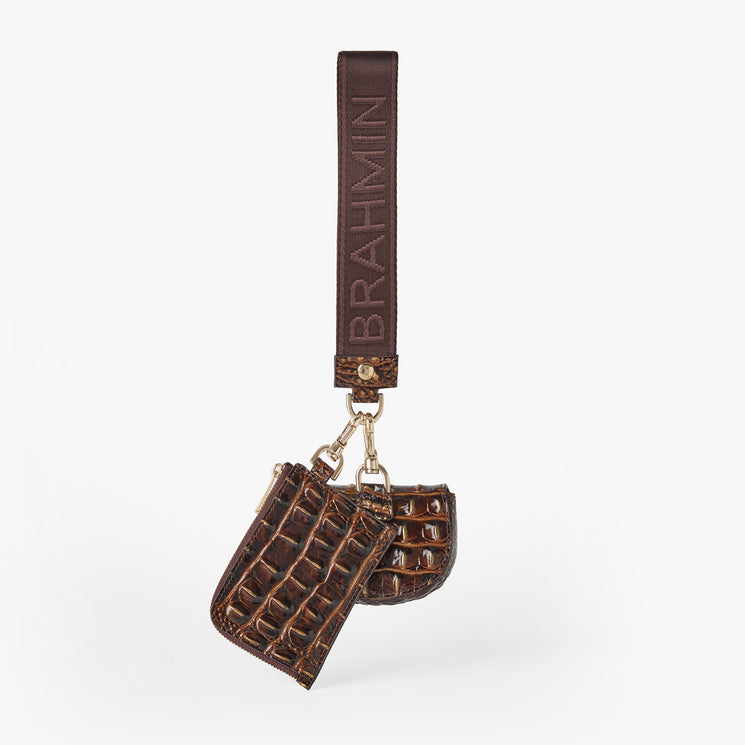 A brown leather keychain bag featuring a crocodile-embossed texture, a matching strap with 'BRAHMIN' printed vertically, and gold-tone hardware, shown against a plain light gray background. Etta back view.