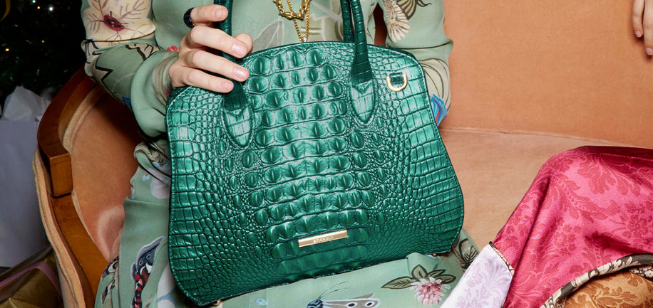 Person holding Mystic Green Melbourne Rosetta Satchel handbag with a floral-patterned chair in the background.