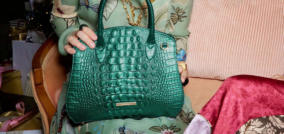 Person holding Mystic Green Melbourne Rosetta Satchel handbag with a floral-patterned chair in the background.