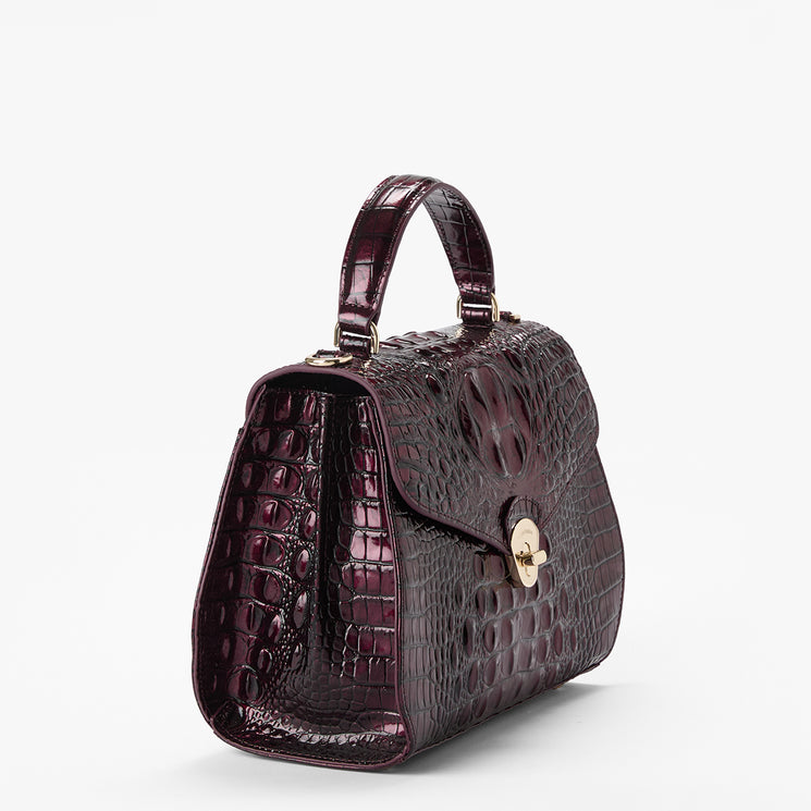 A structured top-handle handbag with a glossy crocodile-embossed texture in deep burgundy, featuring a gold-tone turn-lock closure on the front flap, set against a plain light gray background.