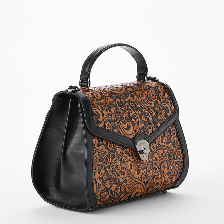 Brown leather handbag with intricate patterns on a white background. Annalise side view.