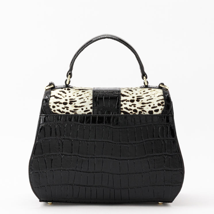 Brahmin Annalise structured black satchel featuring a single top handle, gold-tone hardware, and a black-and-white patterned panel on the turn-lock closure flap, finished with a glossy embossed texture throughout.
