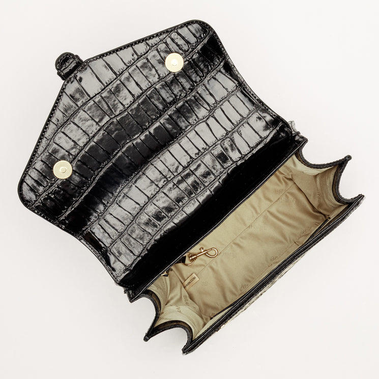 Top-down view of an open black BRAHMIN Annalise satchel in embossed leather, featuring gold-tone magnetic snap closures, a beige interior lining, and a gold-tone lobster claw key clip.