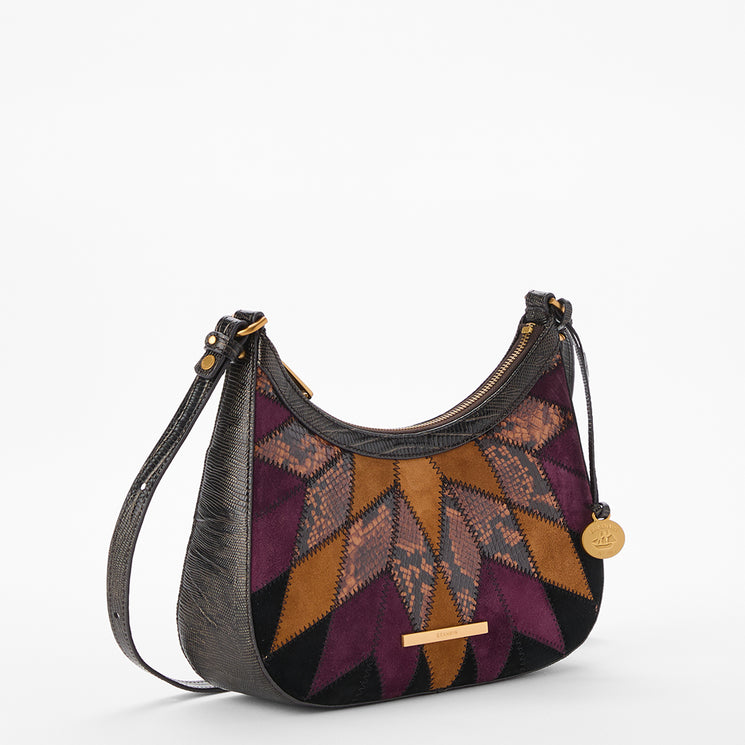 A crescent-shaped shoulder bag with a dark textured leather exterior and a geometric patterned insert in purple, and black. The bag features a matching dark leather strap, gold-tone hardware, and a small round hanging charm on a clean white background.