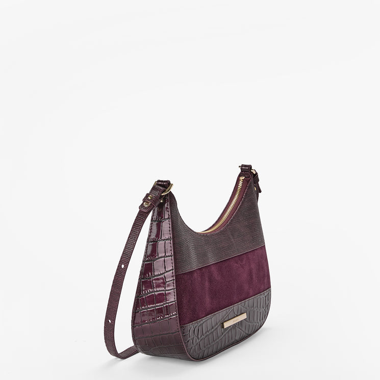 A crescent-shaped shoulder bag in dark purple and brown, featuring crocodile-embossed leather, smooth leather, and suede panels, with a matching shoulder strap and a small gold-tone logo plaque.