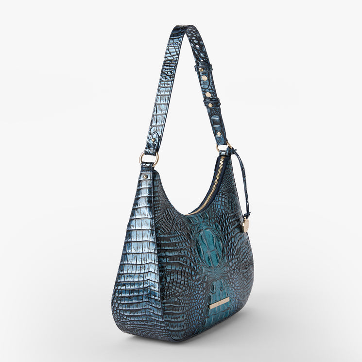 BRAHMIN Stephie crescent shoulder bag in blue with textured, crocodile-embossed pattern, features a short adjustable strap with gold-tone hardware and zip closure; displayed upright against a white backdrop.