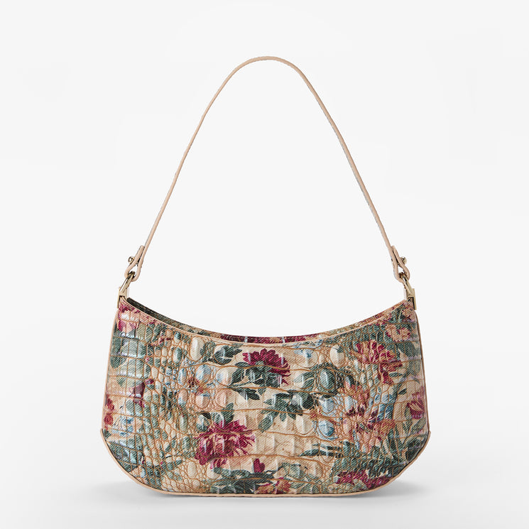 A crescent-shaped shoulder bag with a floral and textured pattern in muted red, green, and beige tones, featuring a thin beige strap and gold-tone hardware, shown against a plain white background.