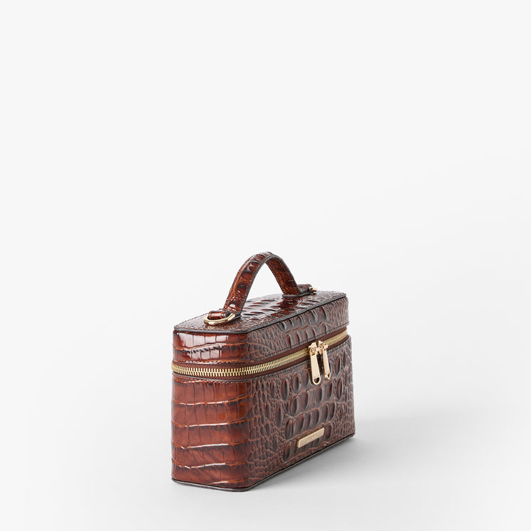 A brown crocodile-embossed leather cosmetic case with a top handle, gold-tone zipper, and a small gold brand plaque on a light gray background. Side view.