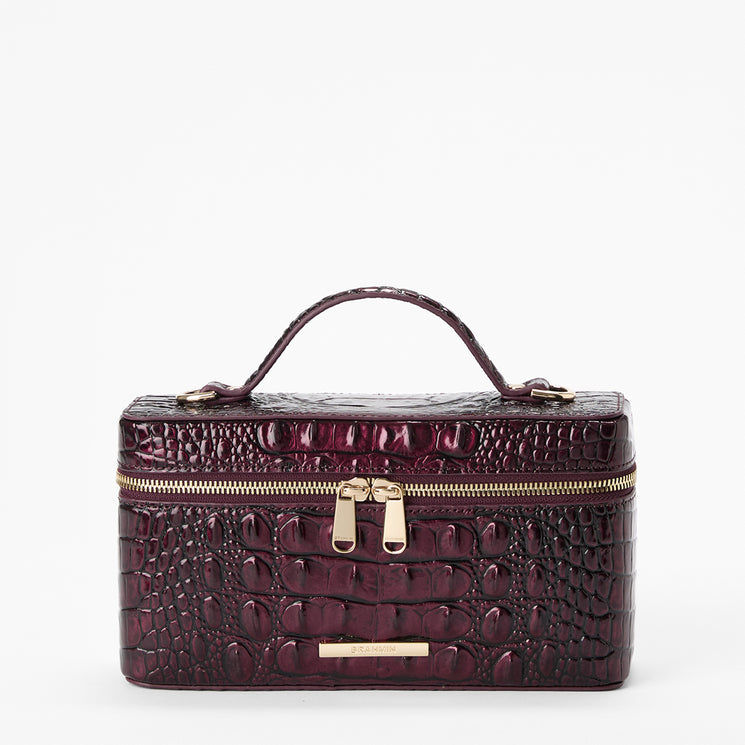 A structured rectangular cosmetic bag with a glossy embossed crocodile pattern in deep burgundy, featuring a top handle, a double zipper closure with gold-tone hardware, and a small gold Brahmin plaque at the bottom front.